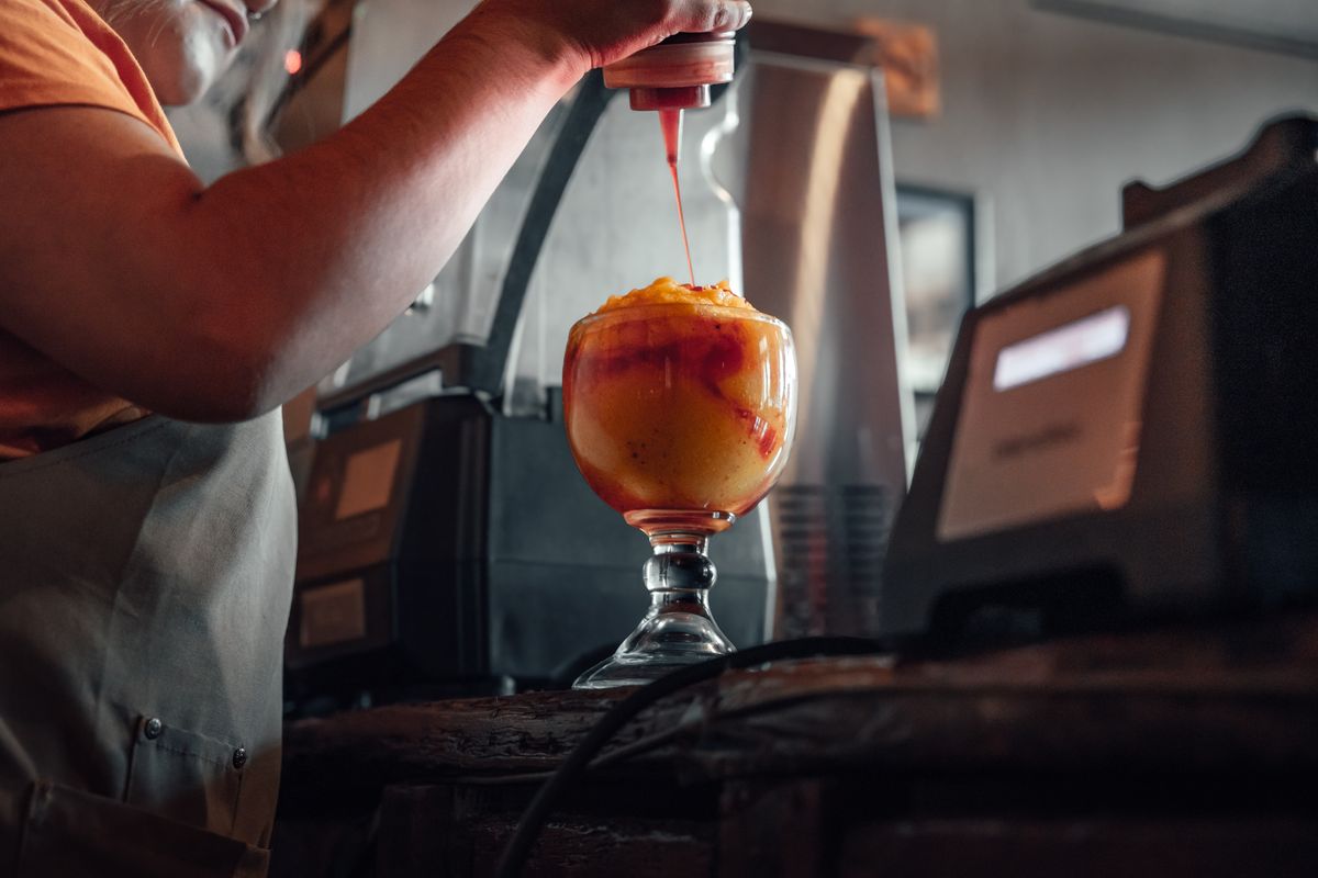 Chamoy being drizzled from a squeeze bottle into a chilli-rimmed glass behind a bar.