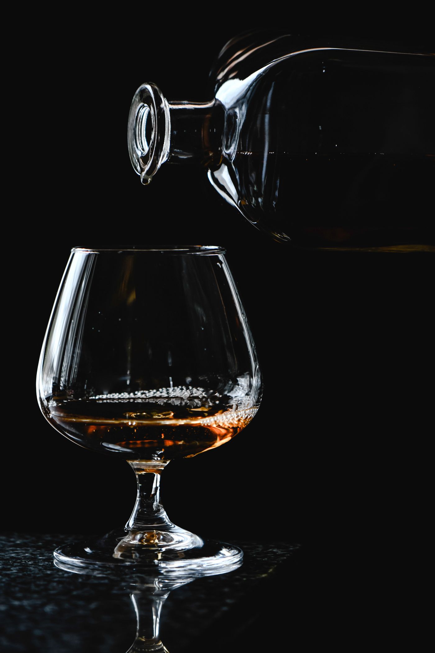 Amber brandy poured from a decanter into a snifter against a black background.