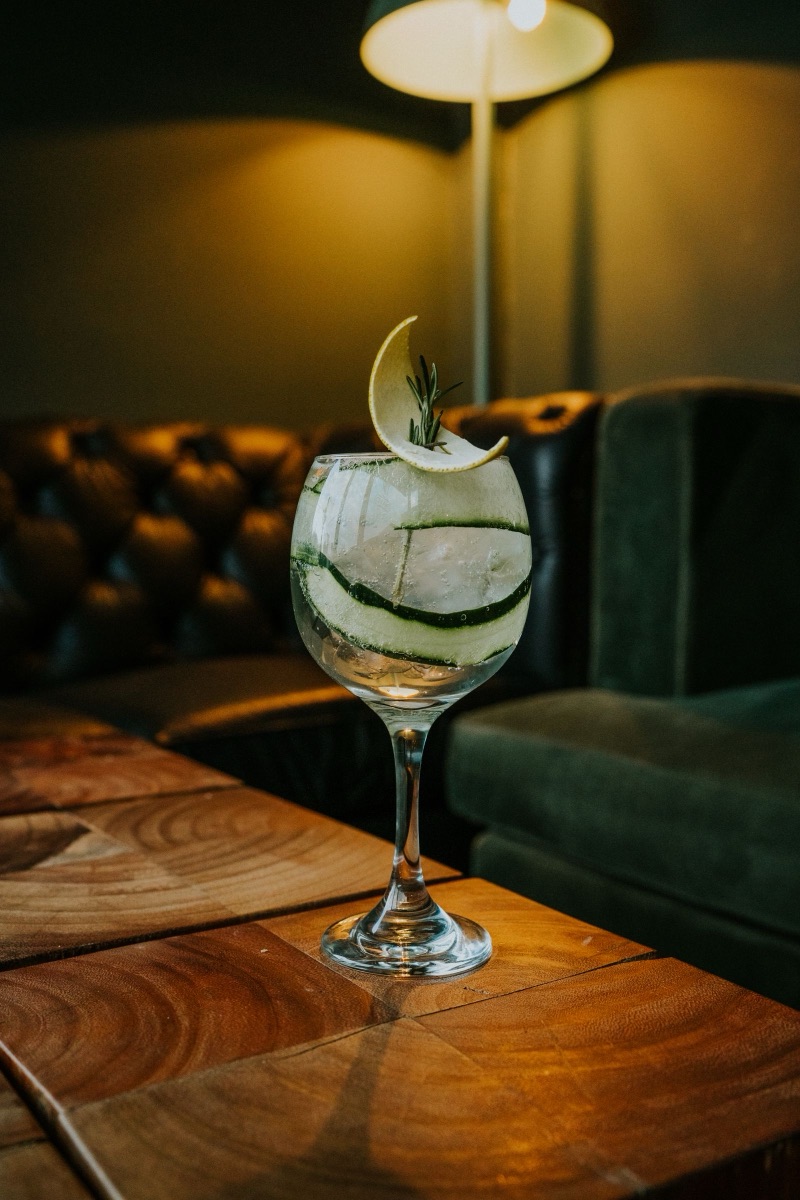 A gin and tonic in a balloon glass with cucumber ribbons and rosemary.