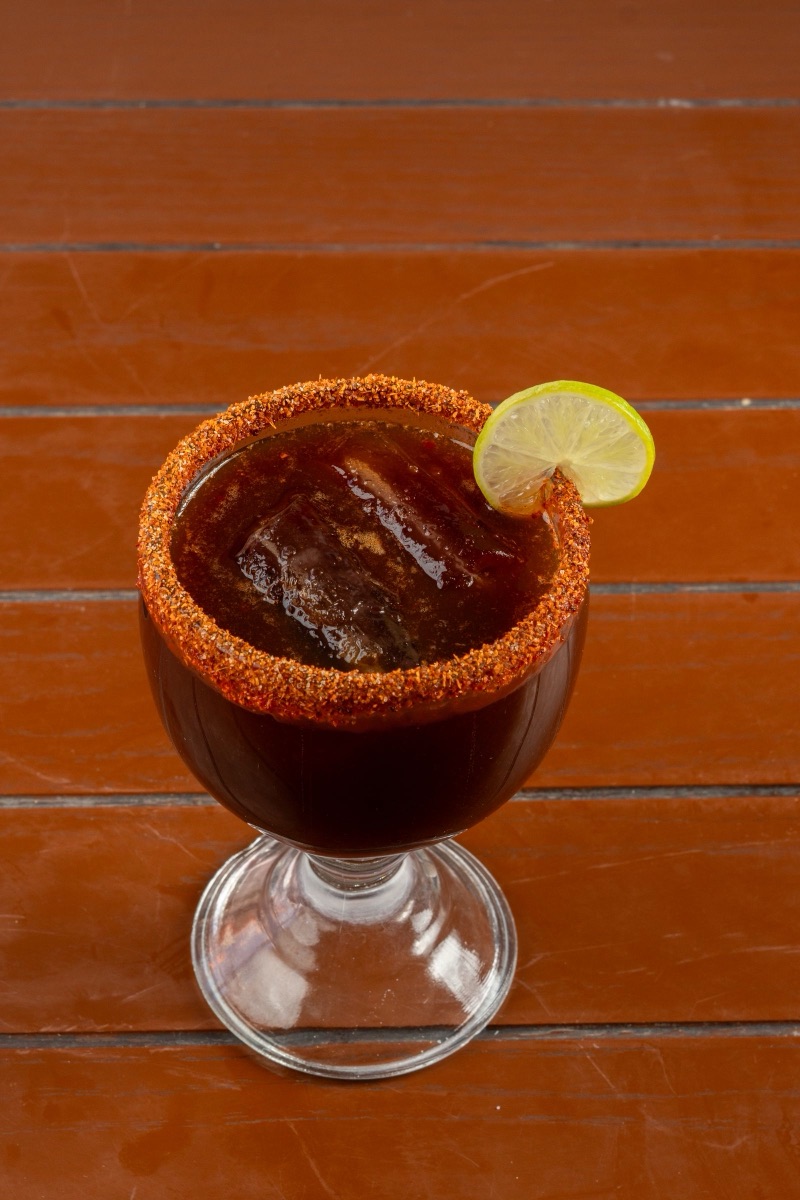 Una michelada en copa con escarchado grueso de chile y sal, y una rueda de limón en el borde.