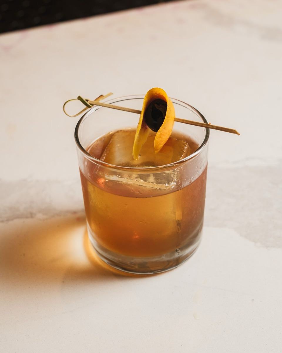 An old fashioned in a rocks glass over one large cube, with an orange twist.