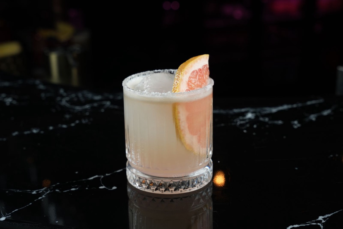 A paloma in a rocks glass with a salted rim and a wedge of pink grapefruit.