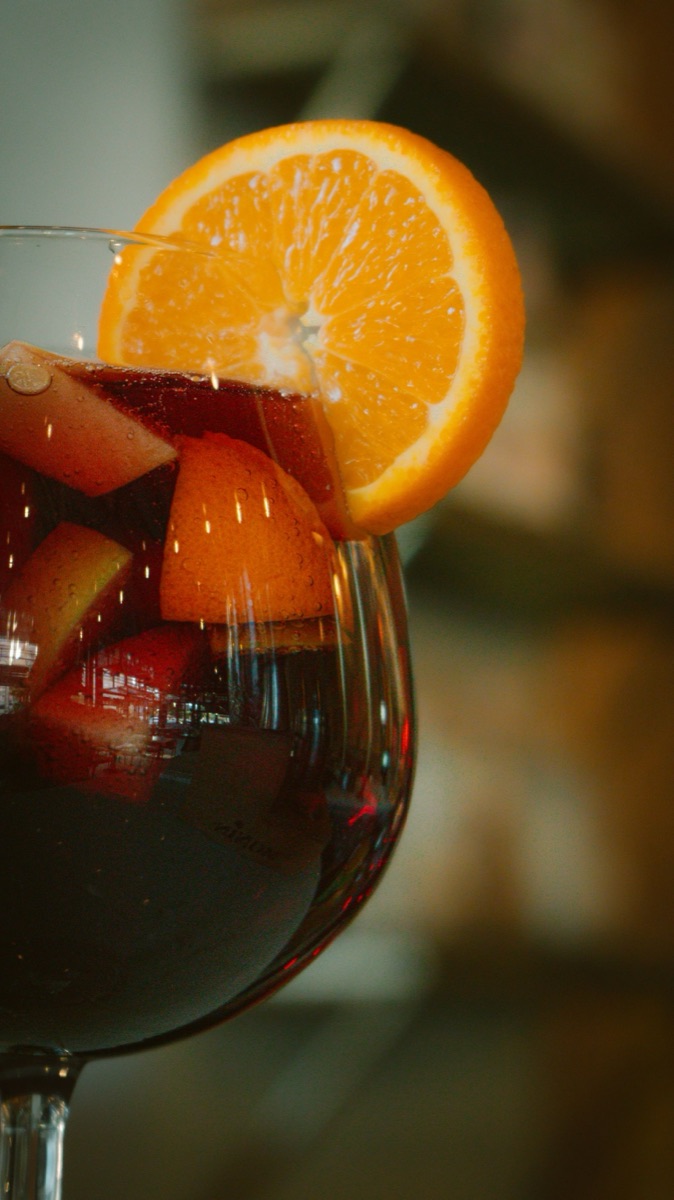 A glass of red sangria loaded with orange and apple slices.