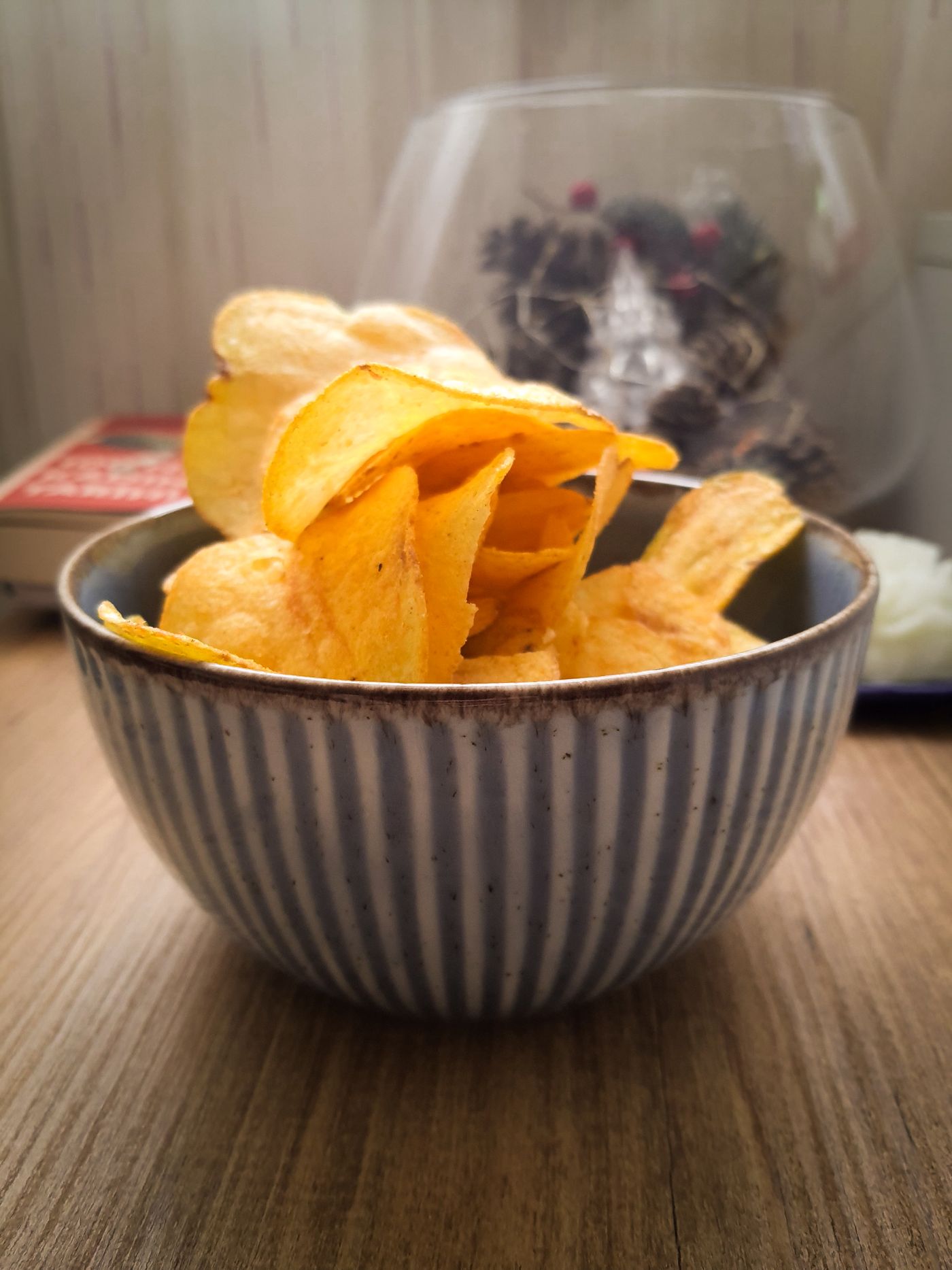 A striped ceramic bowl heaped with golden potato chips on a wooden table.