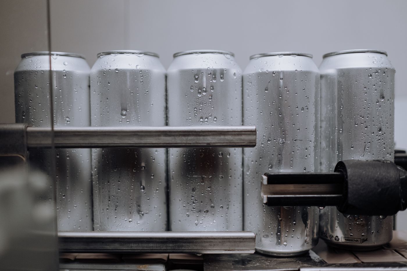 Unlabelled aluminium tallboy cans, beaded with condensation, straight off the cold line.