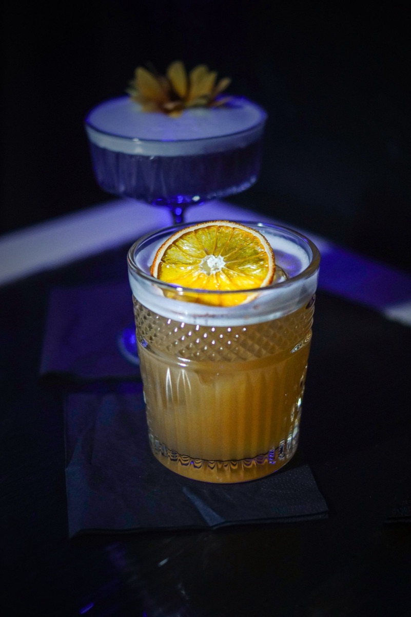 A whiskey sour with a thick foam top and a dried orange wheel.