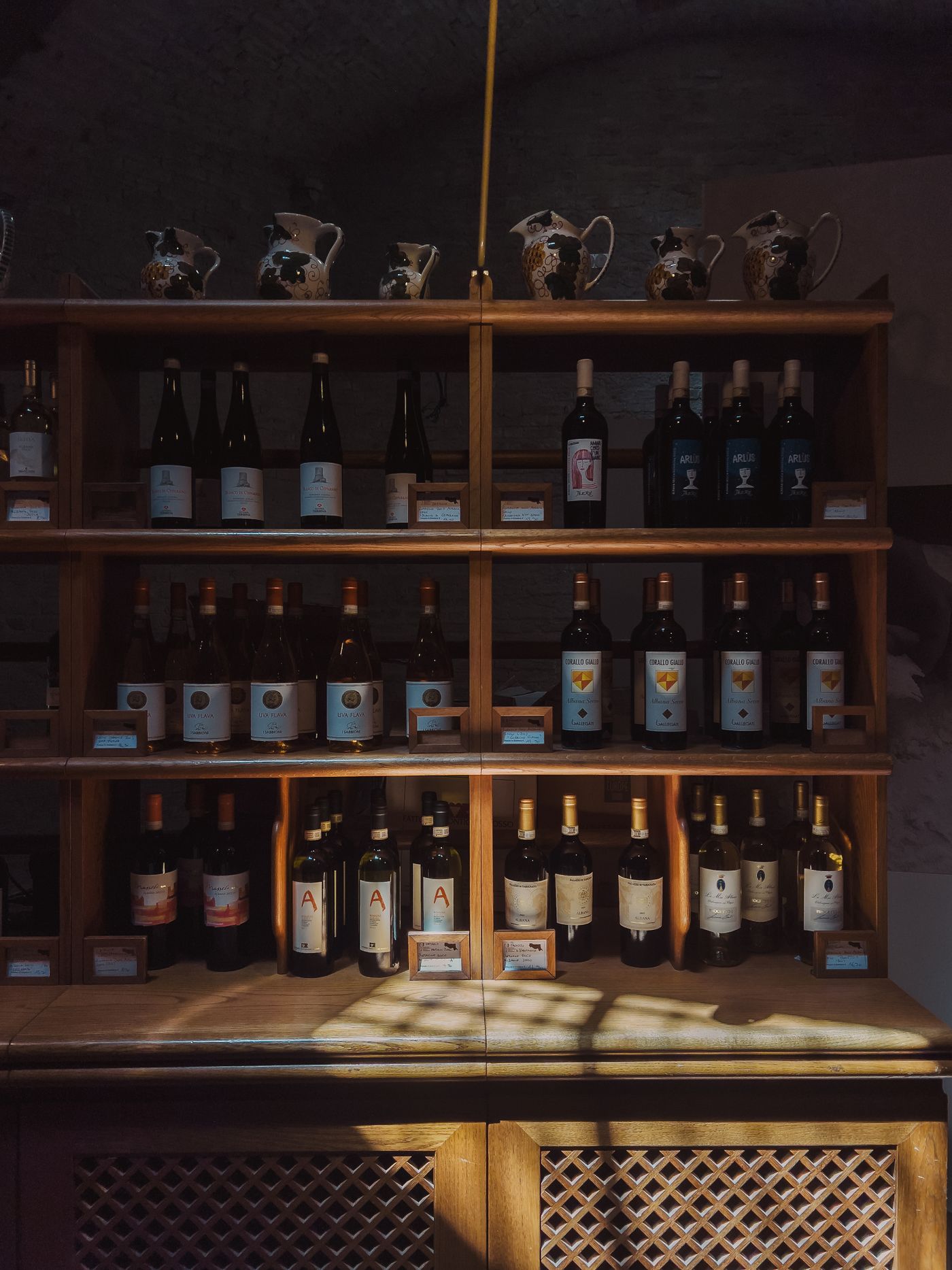 Estantes de madera con vinos tintos y blancos surtidos bajo una luz cálida y tenue.